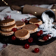 Load image into Gallery viewer, Stack of cherry bakewell welsh cakes with cherries on a rustic surface with a rolling pin and flour container.