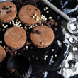 Load image into Gallery viewer, Triple Chocolate Welsh Cakes on a messy griddle with chocolate chips scattered all around, flour and a welsh cake cutter.