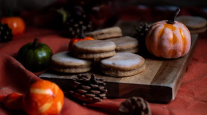 Pumpkin Spice Welsh Cakes on a wooden chopping board surrounded by pumpkins.