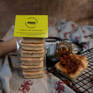 Packaged Cheese and Leek Welsh Cakes with a jar of chutney on kitchen table cloth and cooling rack.