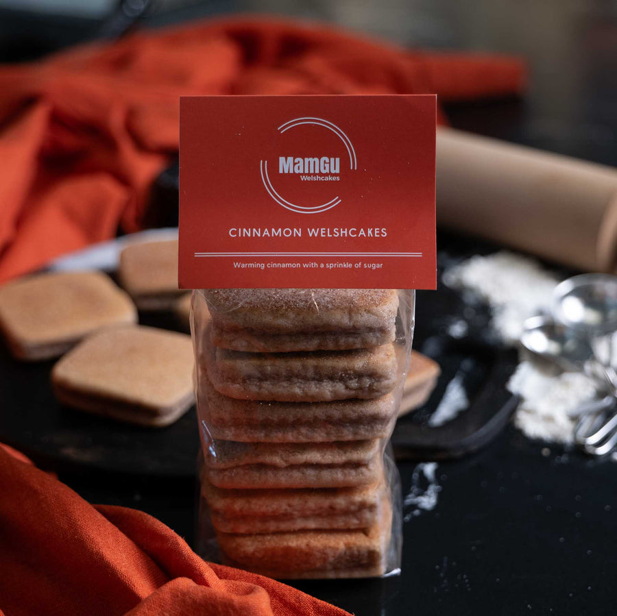 Packaged cinnamon Welsh Cakes with a MamGu Welshcakes label on a messy kitchen worktop