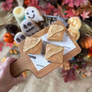 Three Chai flavoured Welsh Cakes with triangle icing on a wooden board with Halloween-themed decorations in the background.