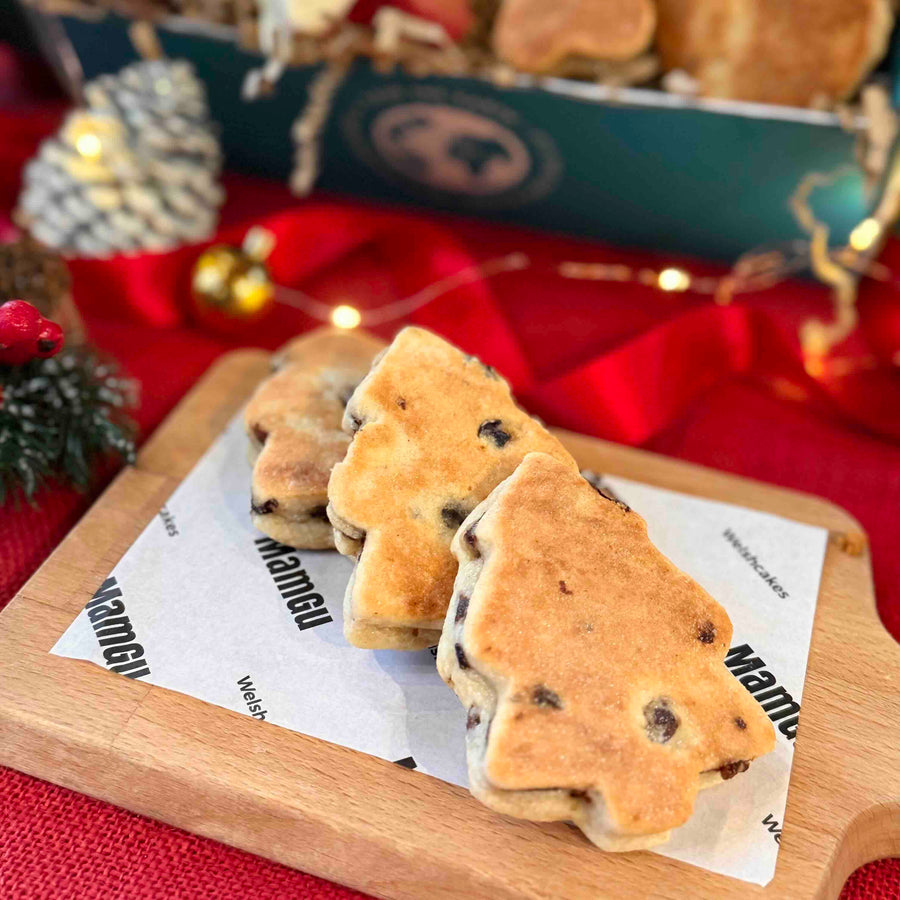 Three Christmas tree Welsh cakes on a wooden board with Christmas decorations in the background