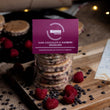 Load image into Gallery viewer, Dark Chocolate &amp; Raspberry Welshcakes in a pack with a purple label on a messy rustic worktop with loose raspberry and chocolate chips
