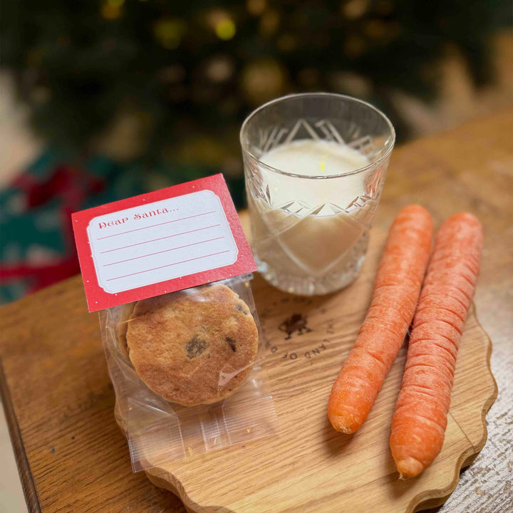 2 pack of traditional welsh cakes with a space for children to write a note or draw a picture for Santa. Displayed on a wooden chopping board with two carrots and milk next to a Christmas tree.