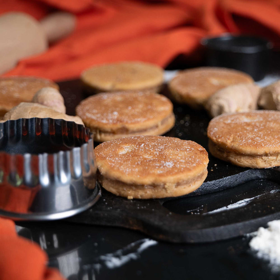 Loose ginger welsh cakes on a black bakestone griddle with a welsh cake cutter and ginger for decoration
