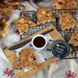 Load image into Gallery viewer, A styled flat-lay of ghost-shaped traditional welshcakes on a wooden board with a small dish of strawberry jam and Daffodil Foods Clotted Cream, set on a patterned cloth with autumn leaves and acorns.
