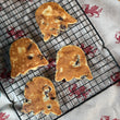 Load image into Gallery viewer, Four ghost-shaped traditional welshcakes resting on a black wire cooling rack over a beige cloth with a red dragon pattern.
