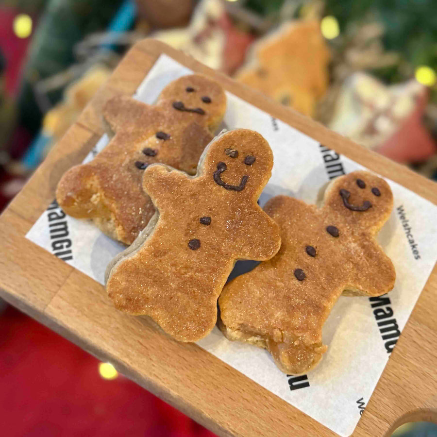 Three gingerbread men welsh cakes on a wooden board with a blurred festive background.