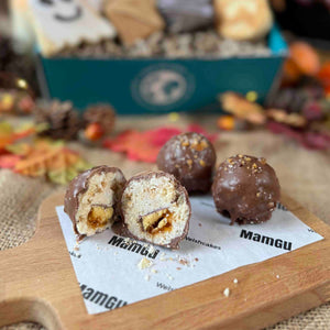 Chocolate-dipped welsh cake treats on a wooden board with 'MamGu Welshcakes' branding, blurred background of more treats and autumn decorations
