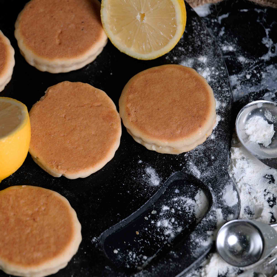 Lemon Welshcakes on a griddle with flour and cut lemons