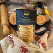 Load image into Gallery viewer, 6 marmite welsh cakes in clear packaging with a black mamgu welshcakes label on top. it is on top of a messy kitchen work top with a rolling pin to the left, a black bakestone in the background, loose welsh cakes and an open jar of marmite.
