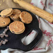 Load image into Gallery viewer, Milk Chocolate Chip Welsh Cakes on a bakestone on a rustic kitchen work top surrounded by chocolate chips and a rolling pin
