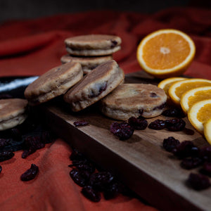 Orange and Cranberry Welsh Cakes on a wooden chopping board with sliced orange and loose cranberries