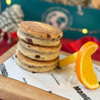 Load image into Gallery viewer, Stack of Welsh cakes with an orange wedge on a branded paper, Christmas-themed background
