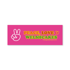 A rectangular pink sticker or label with the text 'PEACE, LOVE & WELSHCAKES' in yellow and green outlined lettering, plus a white peace-sign hand icon on the left. 
