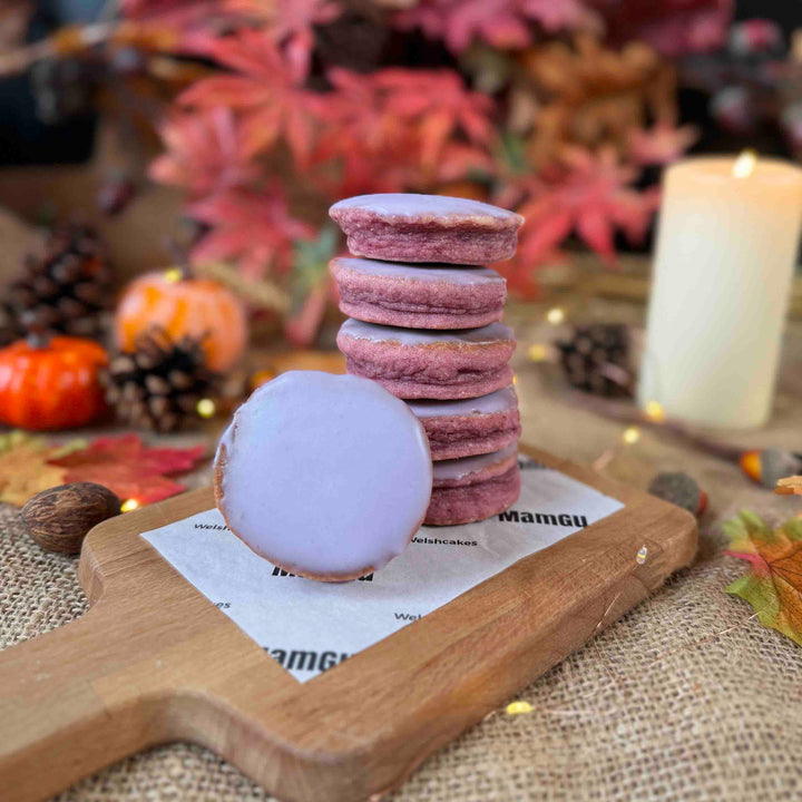 Stack of Purple Parma Violets Welsh Cakes on a wooden board with Autumn-themed decorations in the background.