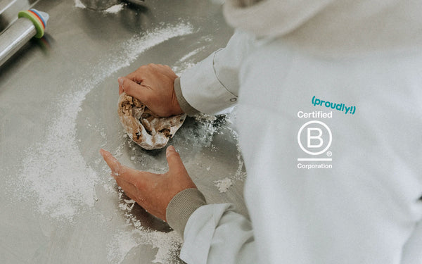 Baker in baker whites kneading dough with a b corp logo on top
