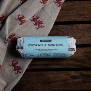 Roll of ready-to-bake Welshcake dough on a wooden surface with a welsh dragon patterned cloth.
