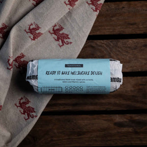 Roll of ready-to-bake Welshcake dough on a wooden surface with a welsh dragon patterned cloth.