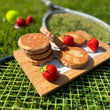 Load image into Gallery viewer, Stack of Strawberries &amp; Cream Welsh Cakes with strawberries on a wooden board on a tennis racket on grass.
