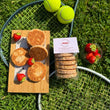 Load image into Gallery viewer, 6 pack of strawberries and cream welsh cakes on a tennis racket, balls, and strawberries on the grass, with loose welsh cakes on a wooden board.
