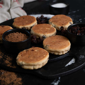 Welsh Cakes on a griddle with ingredients, spices, raisins on the side