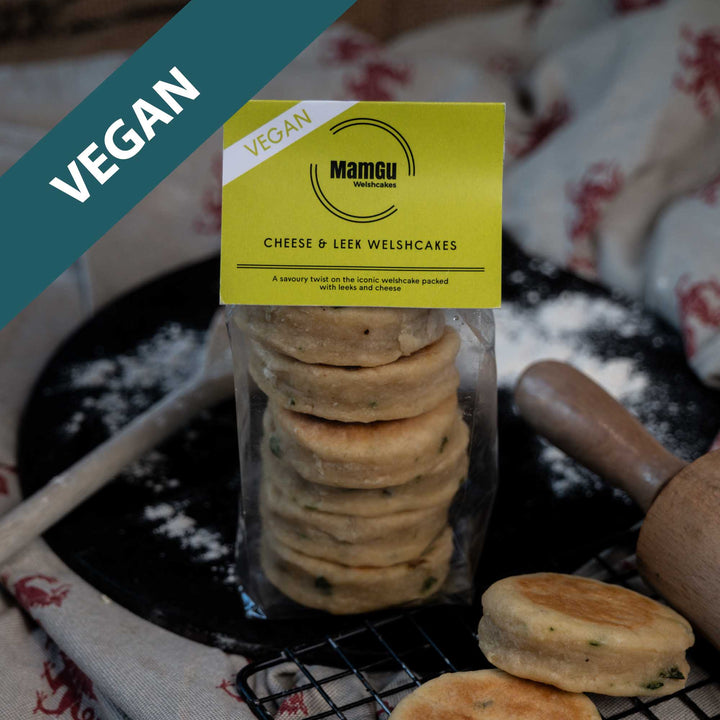 Packaged Vegan Cheese & Leek Welsh Cakes on a busy kitchen work top with rolling pin, wooden spoon, cooling rack and griddle