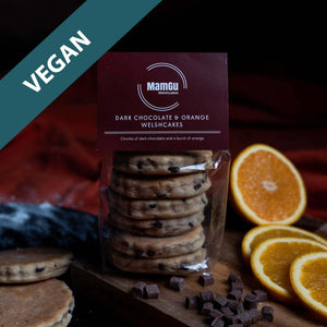 Packaged dark chocolate orange Welshcakes with oranges and chocolate pieces on a wooden board.