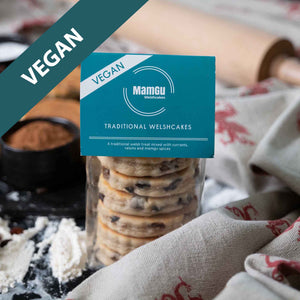 Packaged vegan traditional welsh cakes on a busy work top with welsh dragon table cloth and welsh cake ingredients