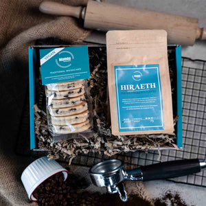 Packaged Traditional Welsh Cakes and ground coffee with branding on a busy kitchen table with rolling pin, cooling rack and coffee beans