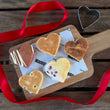 Load image into Gallery viewer, Heart shaped welsh cakes in 5 different flavours on a wooden chopping board surrounded by a red ribbon.
