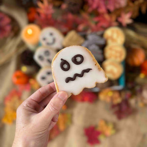 Hand holding a ghost-shaped welsh cake with a blurred Halloween-themed background