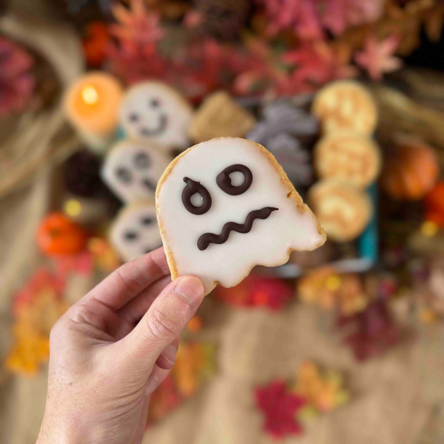 Hand holding a ghost-shaped welsh cake with a blurred Halloween-themed background