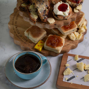 Three-tiered wooden dessert tower with welsh afternoon ingredients and a cup of coffee on a marble surface.