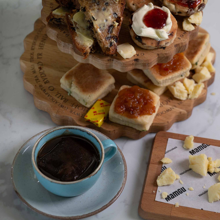 Three-tiered wooden dessert tower with welsh afternoon ingredients and a cup of coffee on a marble surface.