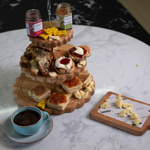 Three-tiered wooden dessert tower with welsh afternoon ingredients and a cup of coffee on a marble surface.