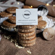 Load image into Gallery viewer, 6 pack of white chocolate chip welsh cakes in clear packaging with a white mamgu welshcakes label. Sitting on a messy rustic kitchen worktop surrounded by ingredients, wooden cutlery and welsh cakes. 
