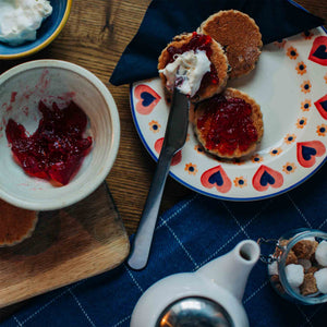 Welsh Cakes with strawberry jam and clotted cream on a decorative plate, surrounded by a bowl of jam and a teapot