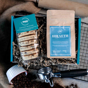 Packaged Traditional Welsh Cakes and ground coffee with branding on a busy kitchen table with rolling pin, cooling rack and coffee beans