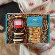 Load image into Gallery viewer, Pack of traditional welsh cakes, jar of jam, and 2 tubs of clotted cream in a blue gift box on a rustic kitchen table
