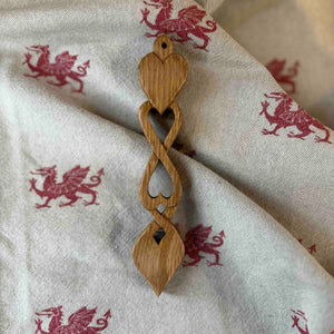 Wooden 6" Welsh Love Spoon on a beige backdrop which has red welsh dragons on it 