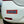 A rectangular red bumper sticker with blue and light blue text reading 'NO WELSHCAKES ARE LEFT IN THIS VEHICLE OVERNIGHT' applied to the rear bumper of a white car.